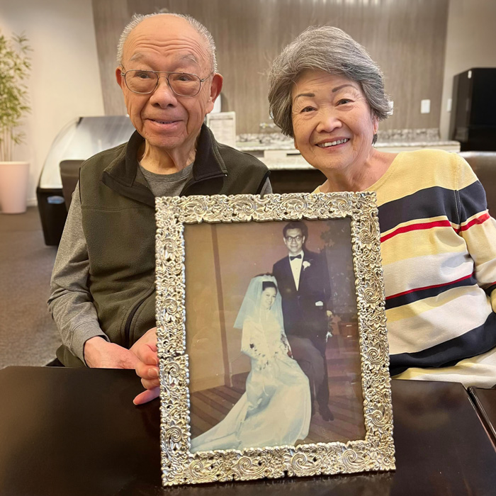 Senior resident couple proudly holding a framed photo of their wedding day, showcasing enduring love and cherished memories, symbolizing a lifetime of togetherness and commitment.