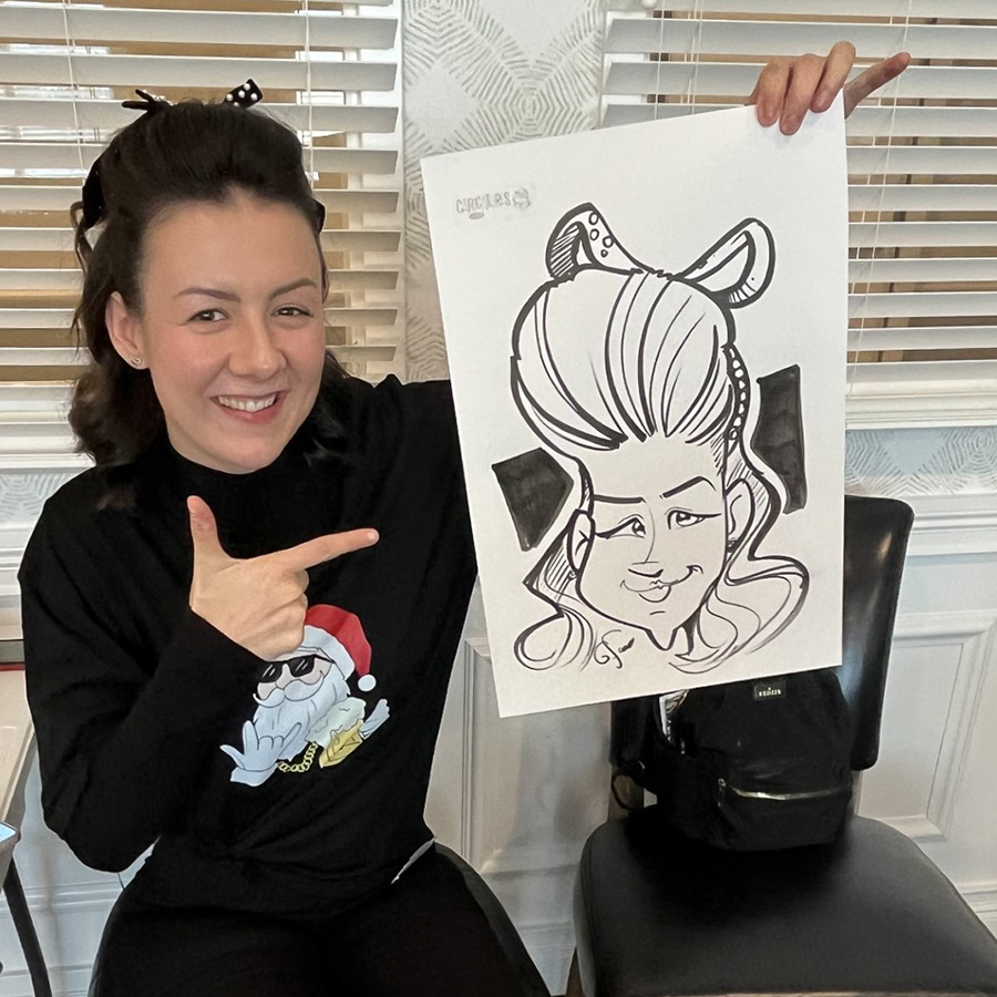 Smiling woman proudly holds up a playful caricature drawing of herself, pointing at the artwork during a fun event at Vitalia North Royalton Senior Living community.
