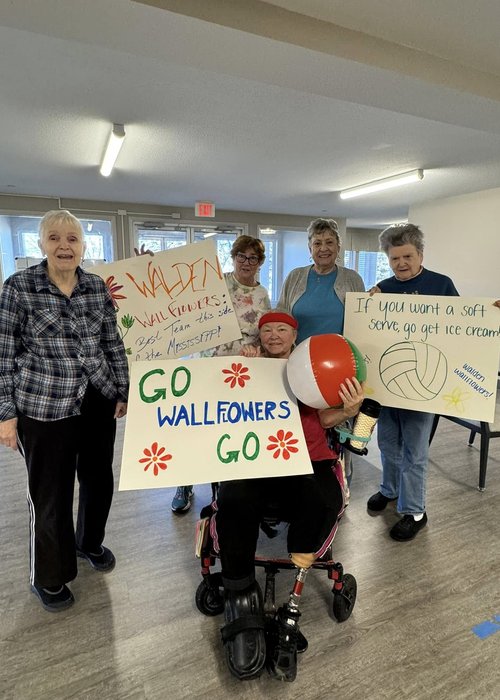 A group of Walden Place Senior Living residents show off colorful handmade posters cheering on their volleyball team.