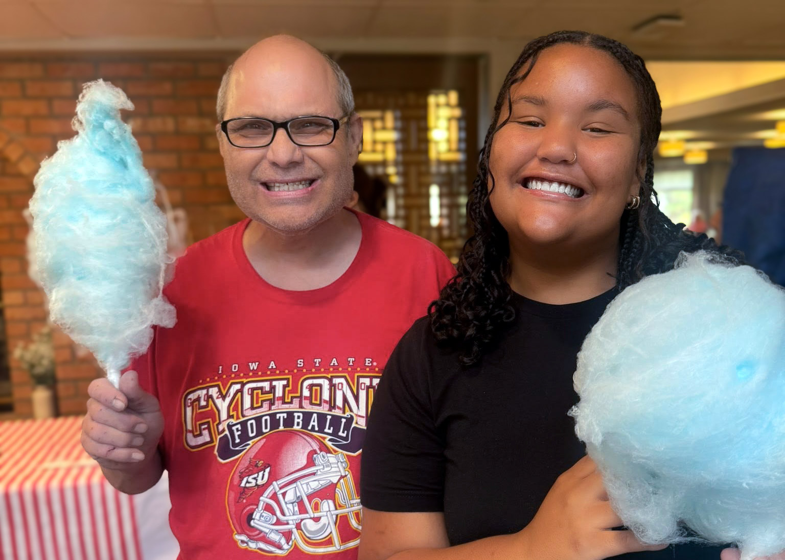 A young woman smiles with a senior man at a community event, both holding a bright blue, freshly spun cotton candy.