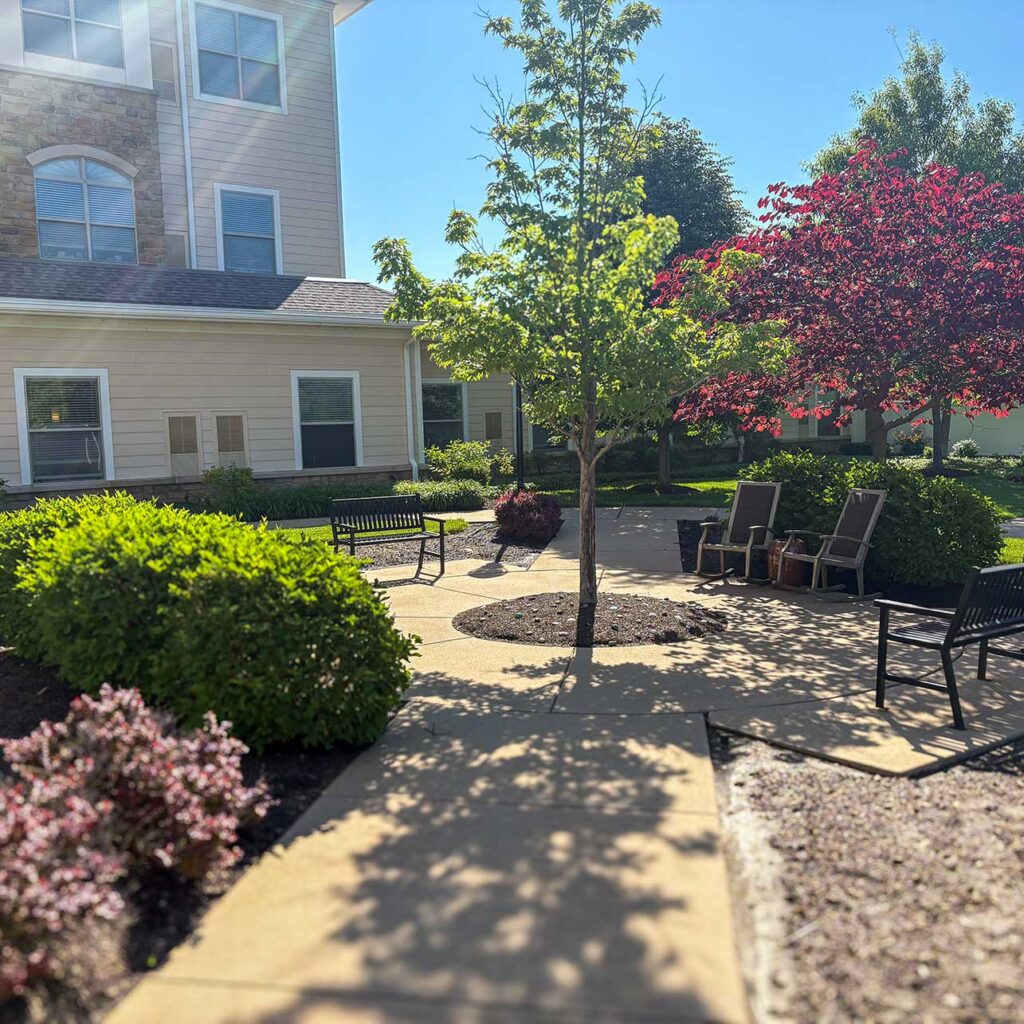 Elegant landscaping at the Henry Senior Living featuring seating, trees and plants of many colors.