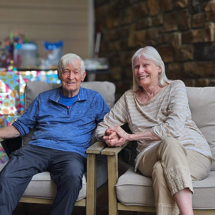 A senior couple smile, seated together, at The Henry Senior Living.